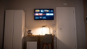 A hotel room with a desk, a television mounted on the wall, a small refrigerator, and a chair. - Toledo Class (Naples)