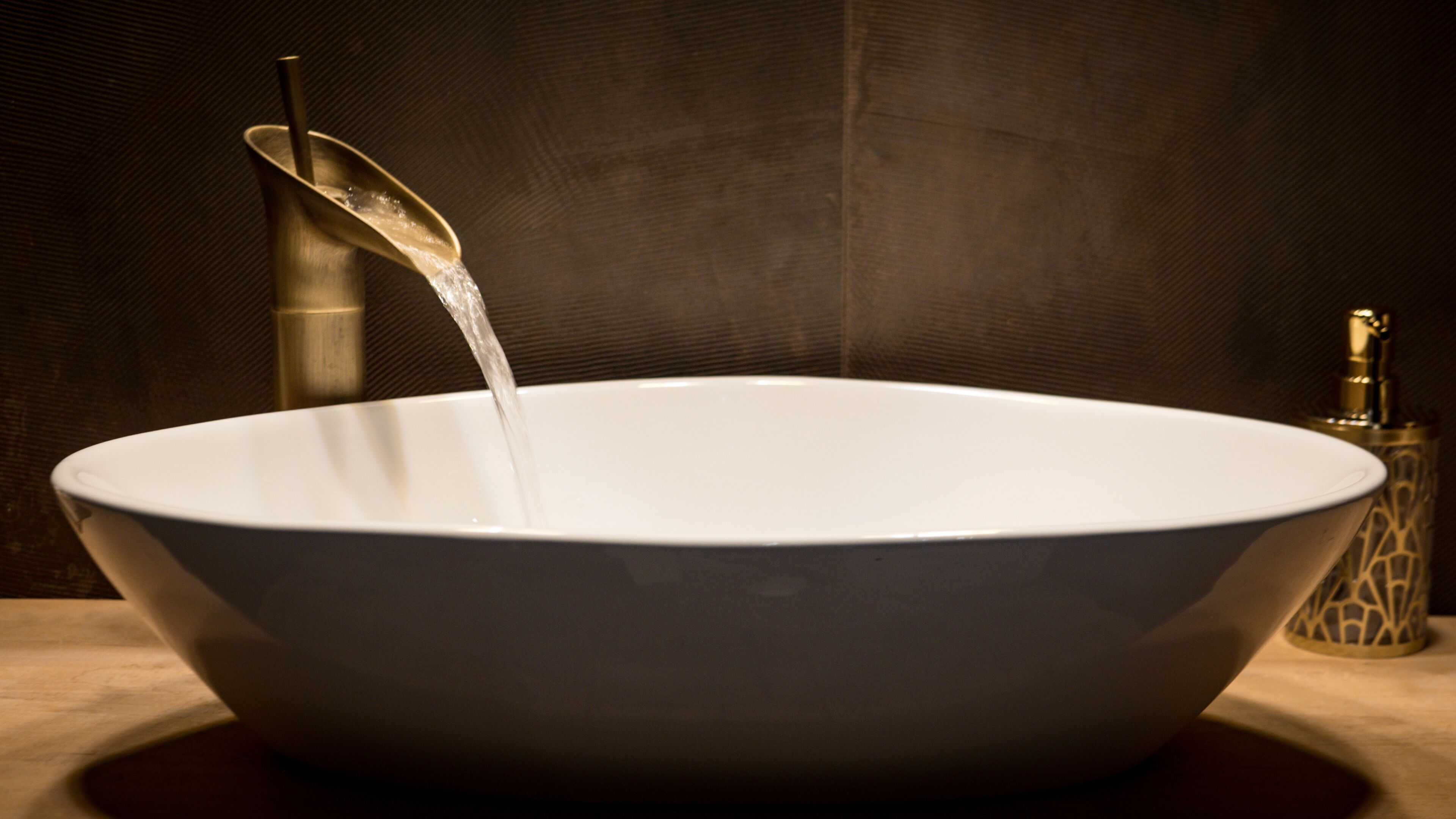 A white ceramic basin with water flowing into it, set against a textured wall.
