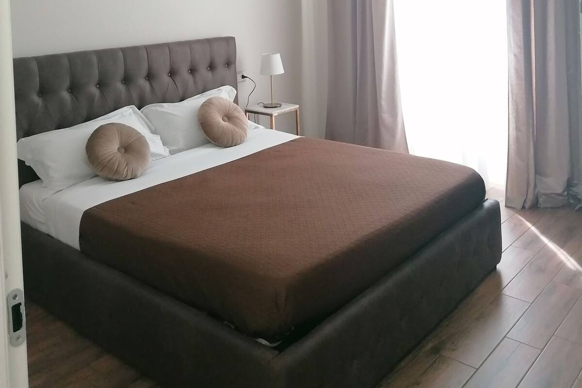 Una cama bien hecha con colcha marrón, cabecera capitonada y dos almohadas.