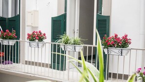 A balcony with white railings and green shutters, potted plants, and a white building facade. - Toledo Class (Naples)