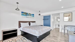 A modern bedroom with a bed, a desk, and a chair. - Tradewinds Motel (Lakewood)