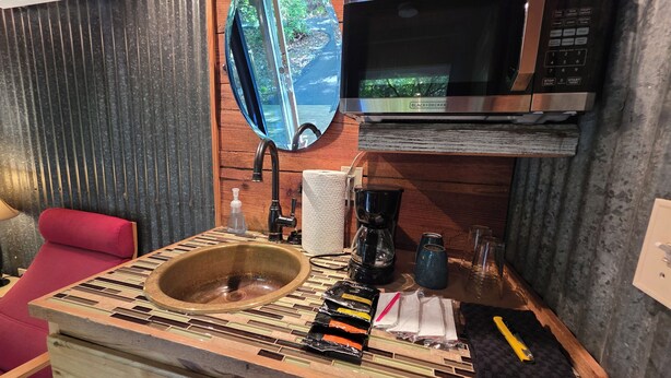 A bathroom with a wooden vanity, a sink, a mirror, a microwave, and a coffee maker.