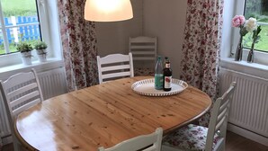 Un coin repas avec une table en bois, des chaises blanches, des rideaux à motifs floraux et un luminaire suspendu.