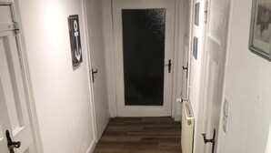 Un couloir étroit avec un plancher en bois, des murs blancs et des portes de chaque côté.