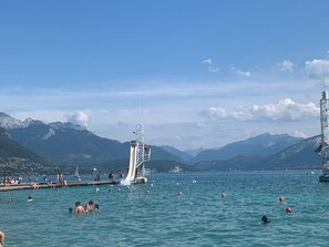 Un lac avec un toboggan aquatique, des gens qui se baignent et des montagnes en arrière-plan.