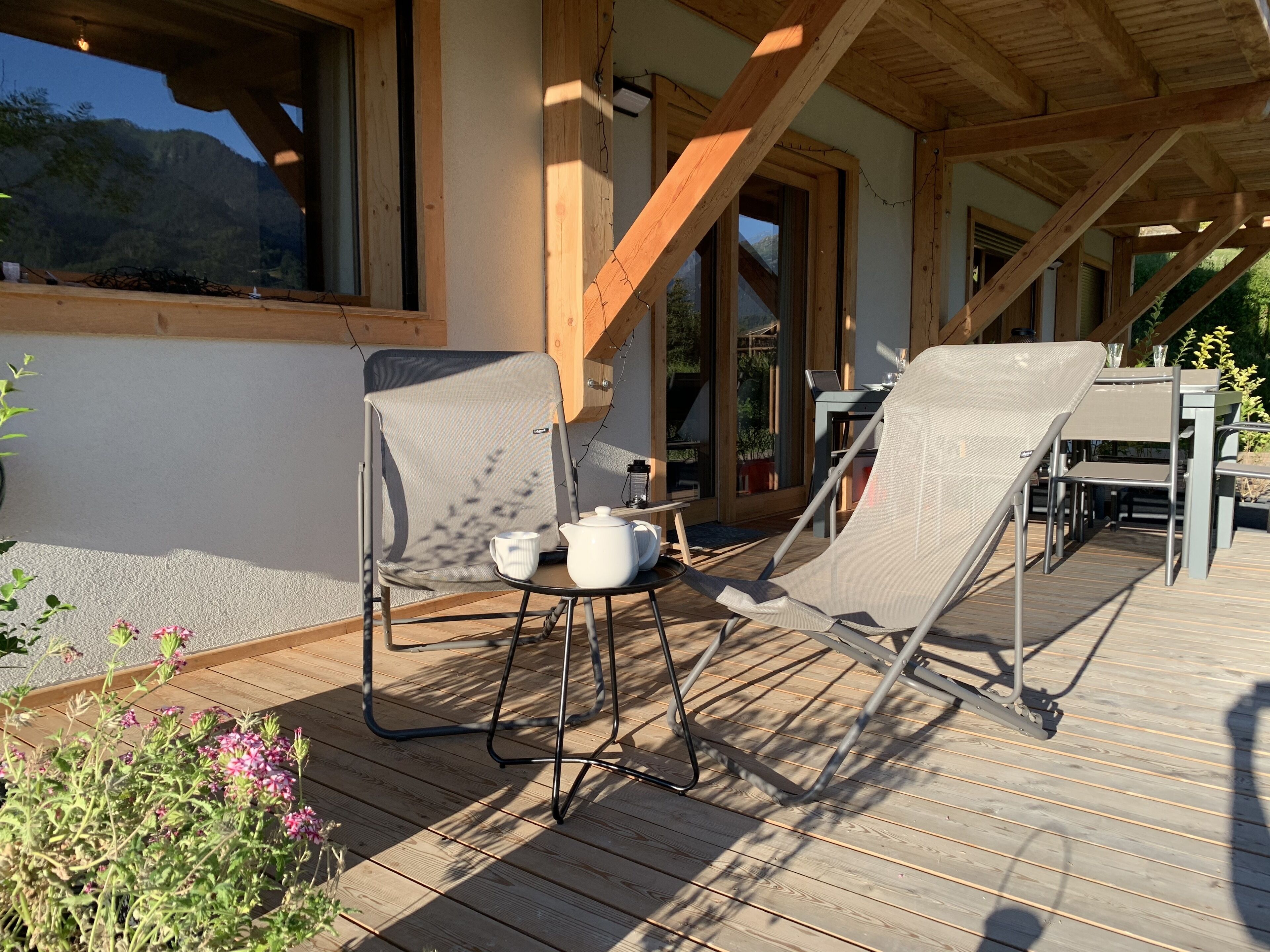Een houten terras met twee loungestoelen, een tafel en een laptop.