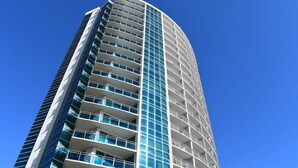 A tall, modern building with a curved facade and numerous balconies.