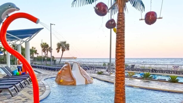 A swimming pool with a dolphin sculpture, palm trees, and a view of the ocean.
