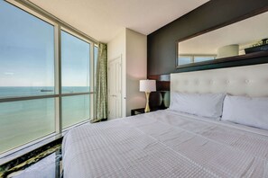 A hotel room with a large window, a bed, a nightstand, and a mirror.