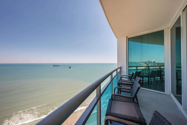 A balcony with wicker furniture, a glass railing, and a view of the ocean.