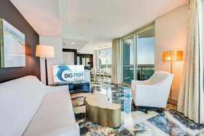 Una habitación de hotel moderna con un ventanal grande, un televisor de pantalla plana, un sofá blanco, un sillón blanco y un suelo de mármol.