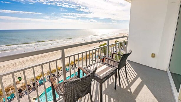 Ein Balkon mit Korbstühlen mit Blick auf Strand und Pool.