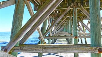 Una estructura de madera de muelle con vista despejada al océano y a la playa arenosa.