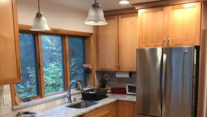 A kitchen with granite countertops, wooden cabinets, a stainless steel refrigerator, and a window with a view of greenery. - Expansive Lakehouse with Jacuzzi (Argyle)