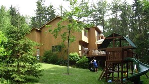 A wooden play structure with a slide and a small tree in a grassy area. - Expansive Lakehouse with Jacuzzi (Argyle)