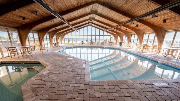 An indoor swimming pool with a brick floor and wooden ceiling, surrounded by tables and chairs. - Oceanfront Corner, Low Floor, Ocean Annies, Pools! (Myrtle Beach)