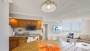 A modern kitchen with wooden cabinets, a microwave, and a dining area with a wooden table and chairs. - Oceanfront Corner, Low Floor, Ocean Annies, Pools! (Myrtle Beach)