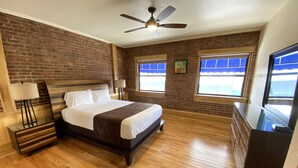 Une chambre avec un mur en briques, un lit, un ventilateur de plafond et une commode.
