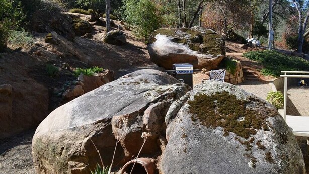 Un espace extérieur rocheux, équipé d’un barbecue et d’un panneau indicateur, entouré d’arbres et de végétation.