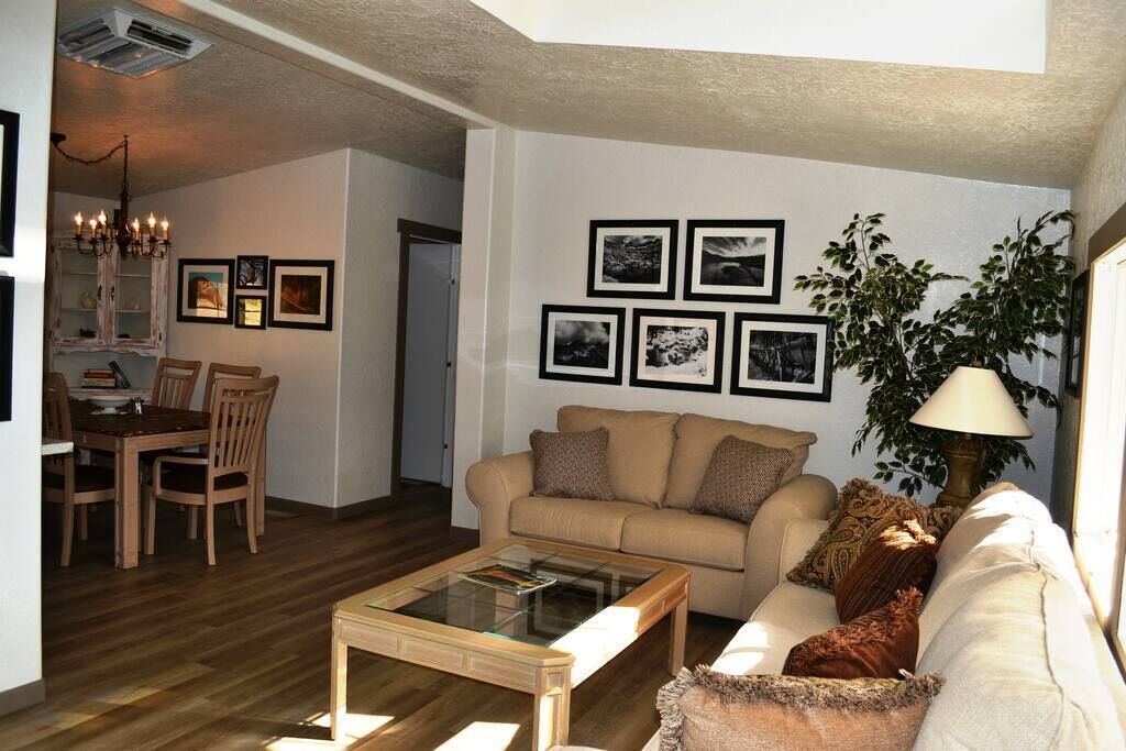Una sala de estar con un sofá color beige, una mesa de centro de vidrio y una zona de comedor con muebles de madera.