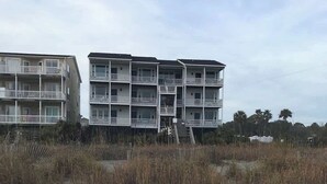 Een gebouw aan het strand met meerdere balkons en een trap naar de verdiepingen.
