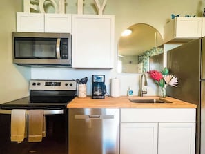 A kitchen with a microwave, stove, coffee maker, sink, and cabinets.