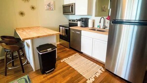 Een kleine keuken met een houten bar, roestvrijstalen apparatuur en een witte achterwand.