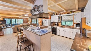 Een ruime keuken met een centraal eiland, witte keukenkastjes en een groot raam.