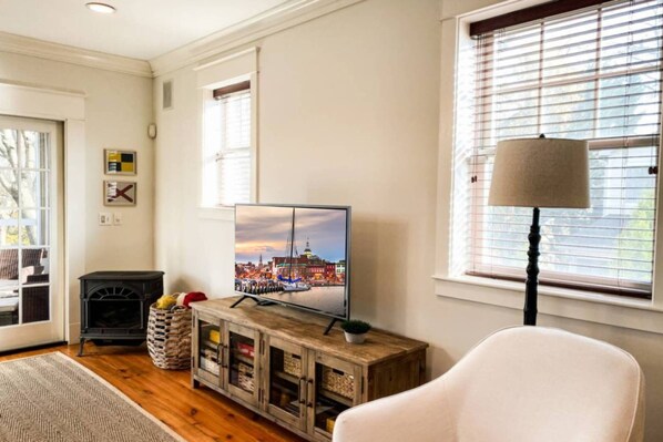 A living room with a television displaying a cityscape, a fireplace, a lamp, and a white chair.