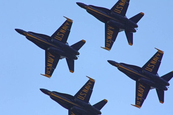 Fyra amerikanska flottans flygplan flyger i formation mot en klar himmel.
