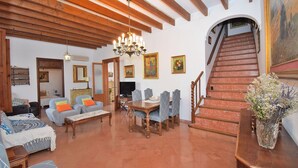 A spacious living room with a dining area, a staircase, and a chandelier.