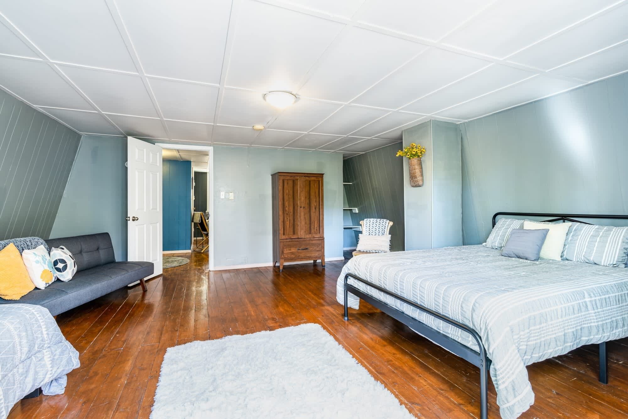 A bedroom with a bed, a sofa, a wooden wardrobe, and a small table.