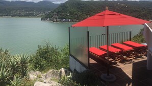 A terrace with red chairs and an umbrella overlooking a lake, surrounded by greenery and hills. - LAS VISTAS HOUSE. Special offer. Landscape, tranquility, comfort, location (Valle de Bravo)