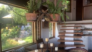 A dining area with a round wooden table, chairs, hanging planters, and a view of the garden through large windows. - LAS VISTAS HOUSE. Special offer. Landscape, tranquility, comfort, location (Valle de Bravo)