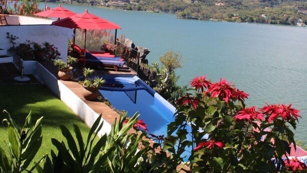 A poolside area with red umbrellas, lounge chairs, and potted plants. - LAS VISTAS HOUSE. Special offer. Landscape, tranquility, comfort, location (Valle de Bravo)