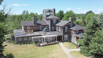 Une grande maison à étages, dotée d’une imposante cheminée en pierre, d’un porche abrité et d’une pelouse bien entretenue.