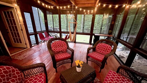A cozy room with wicker furniture, a wooden floor, and large windows with string lights.