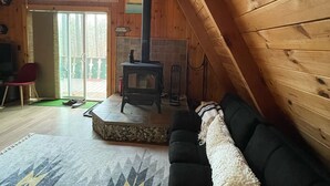 A cozy cabin interior with a black sofa, a patterned rug, a fireplace, and a large window.