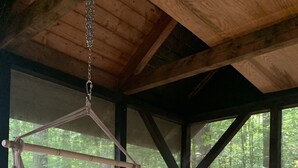A hammock suspended from a ceiling, a red chair, and a large window with a view of a forested area.