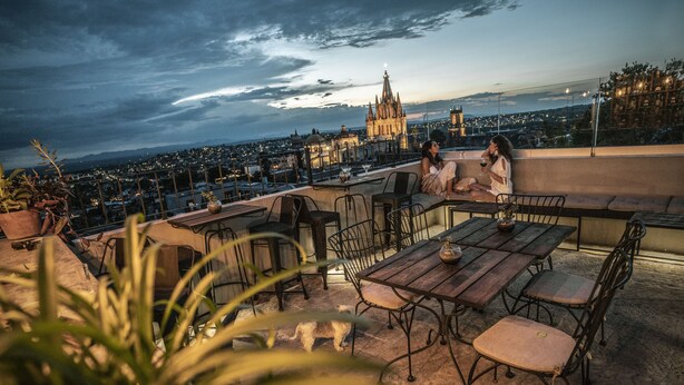 A rooftop terrace with a view of a cathedral, outdoor seating, and a small dog. - Clandestino Hotel Recreo - Adults Only (San Miguel de Allende)