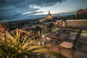 Une terrasse sur le toit offrant une vue sur une cathédrale, des sièges en plein air et un petit chien.