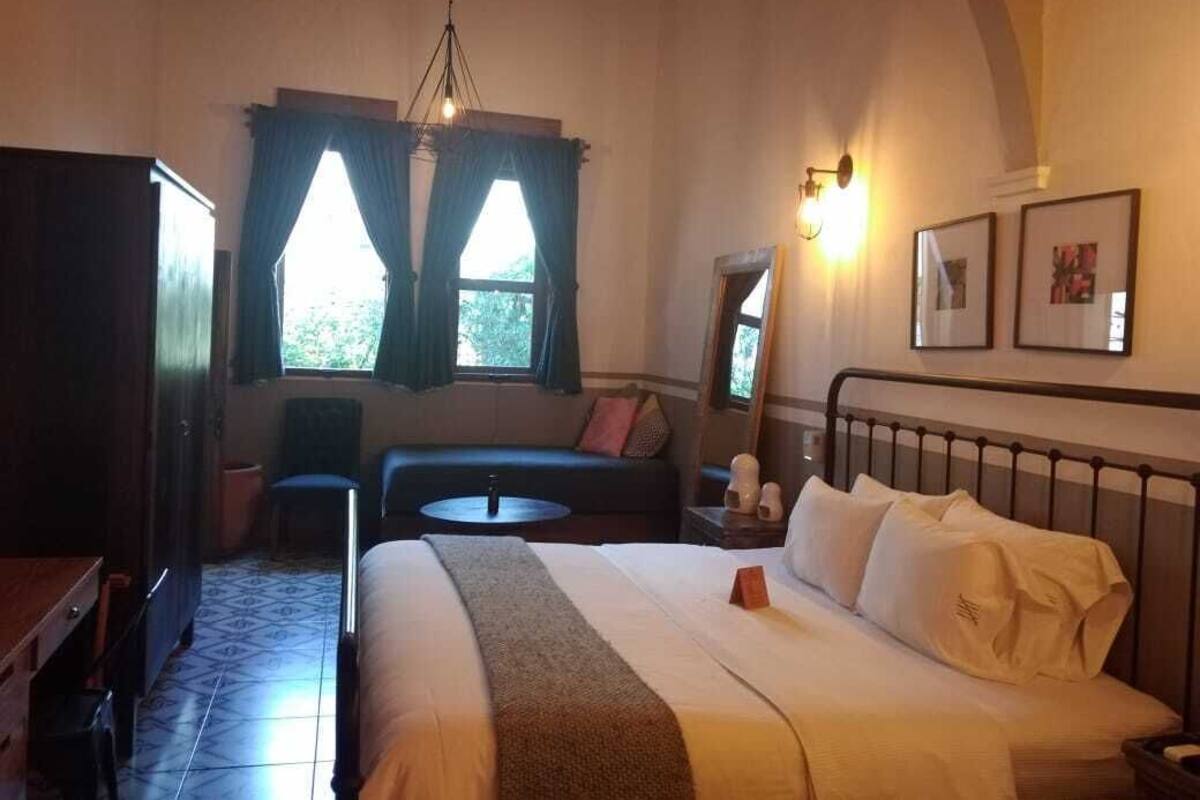 Une chambre à coucher avec un lit, un bureau, une chaise, une petite table et une fenêtre avec des rideaux.