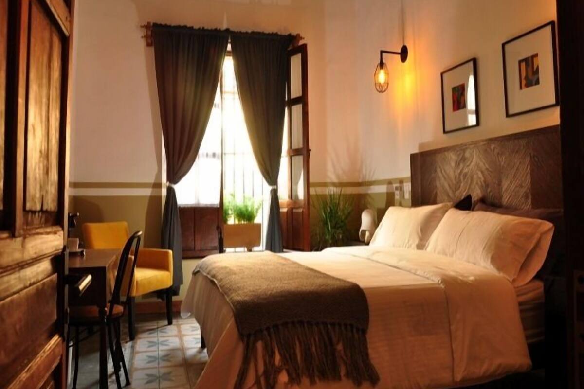 Une chambre d’hôtel avec un lit, un bureau, une chaise et une fenêtre avec des rideaux.