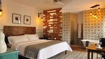 A bedroom with a wooden headboard, a bed with white linens, a wooden partition, a bathroom with a bathtub, and patterned wallpaper.