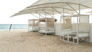 Un espace de cabanes de plage avec des structures métalliques blanches et un auvent offrant de l’ombre.