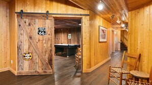 A wooden interior with a pool table, a door labeled "Route 66," and a chair.