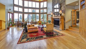 A spacious living room with a fireplace, large windows, and a high ceiling.