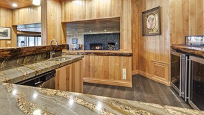 A kitchen with wooden paneling, a stone fireplace, a granite countertop, and a dishwasher.
