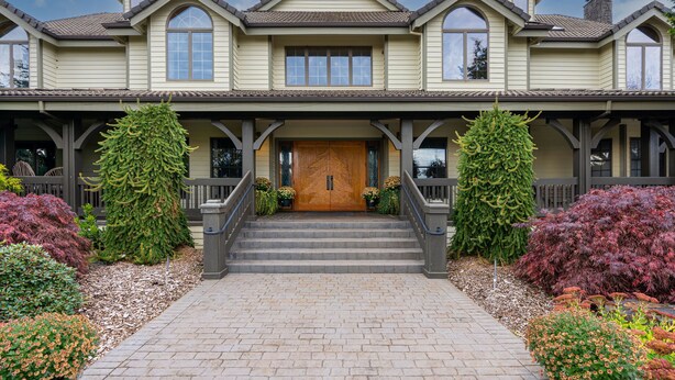 A large, two-story house with a prominent front door, a covered porch, and a brick pathway leading to the entrance.