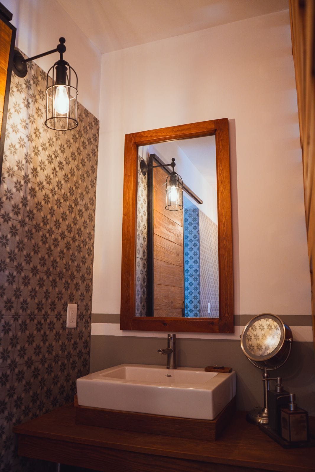 Un baño con un espejo de marco de madera, un lavabo blanco y una lámpara fijada a la pared.
